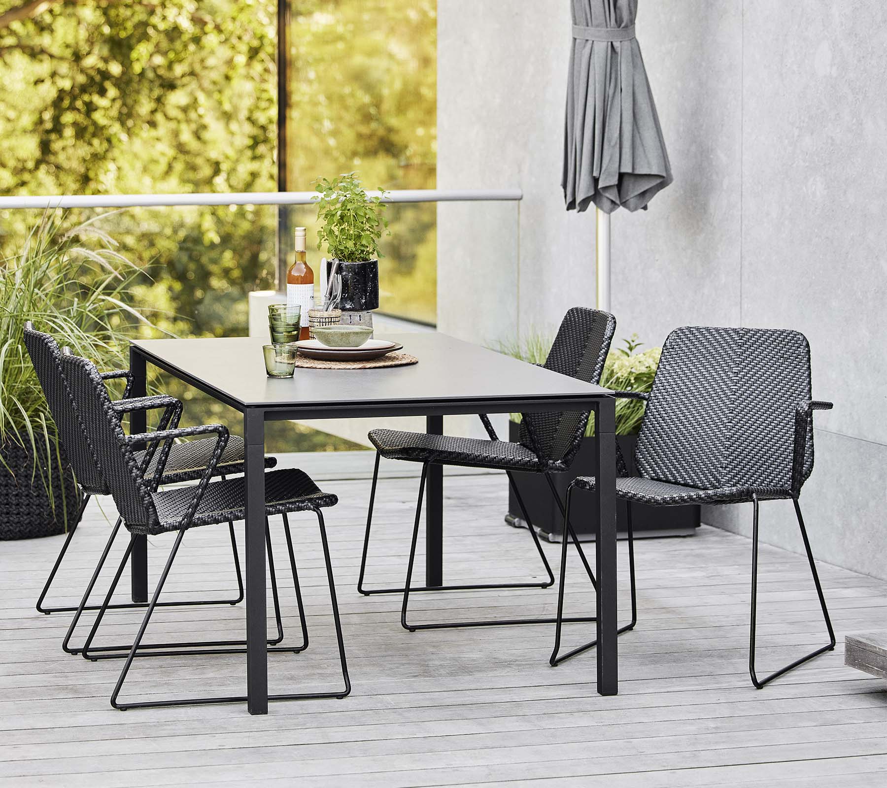 Una mesa moderna rodeada de sillas elegantes, complementada con elementos decorativos y vegetación en el fondo.