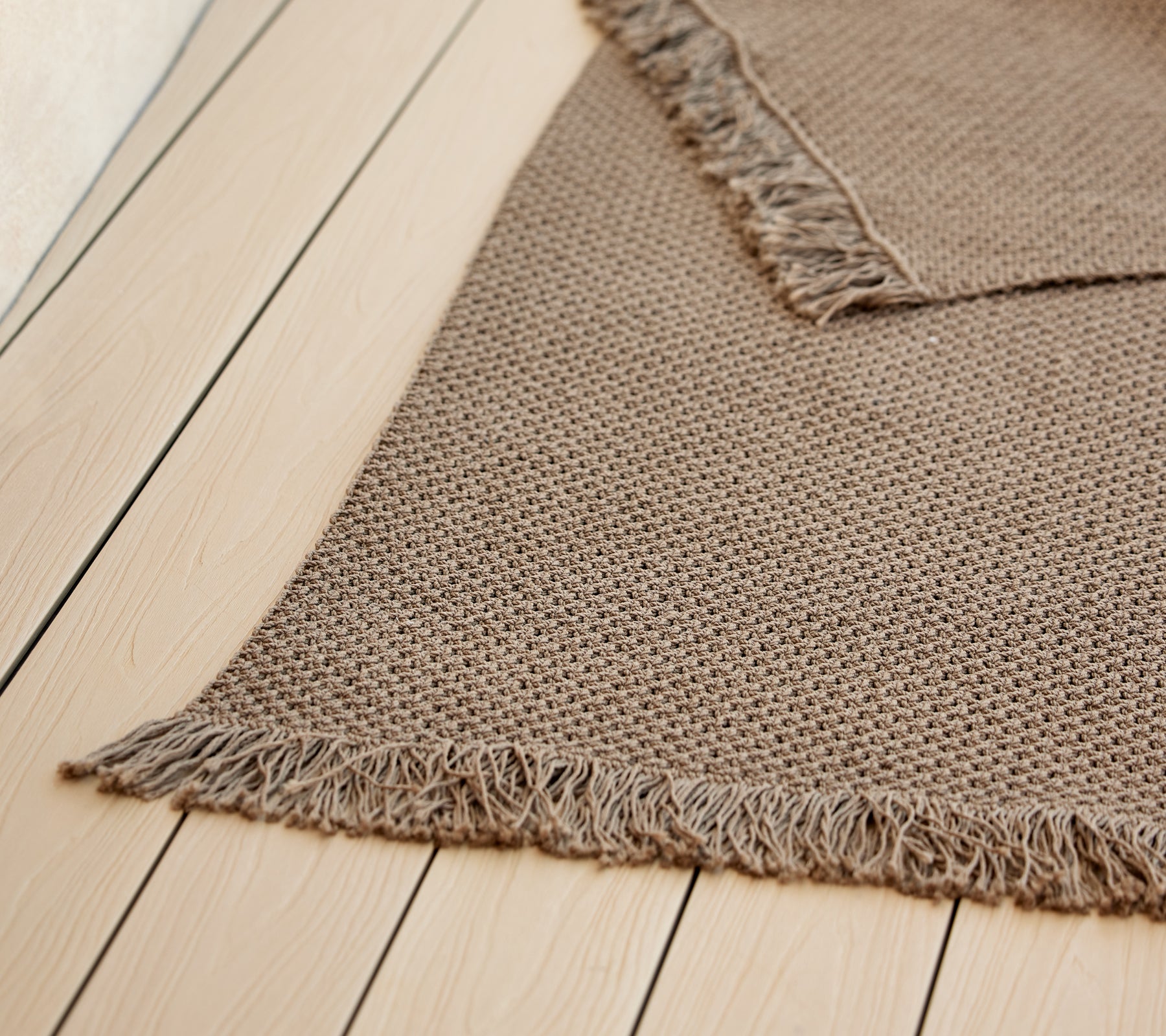 Una alfombra de punto texturizada con bordes flecos, que muestra un color cálido y neutro, mejorando su estética acogedora.