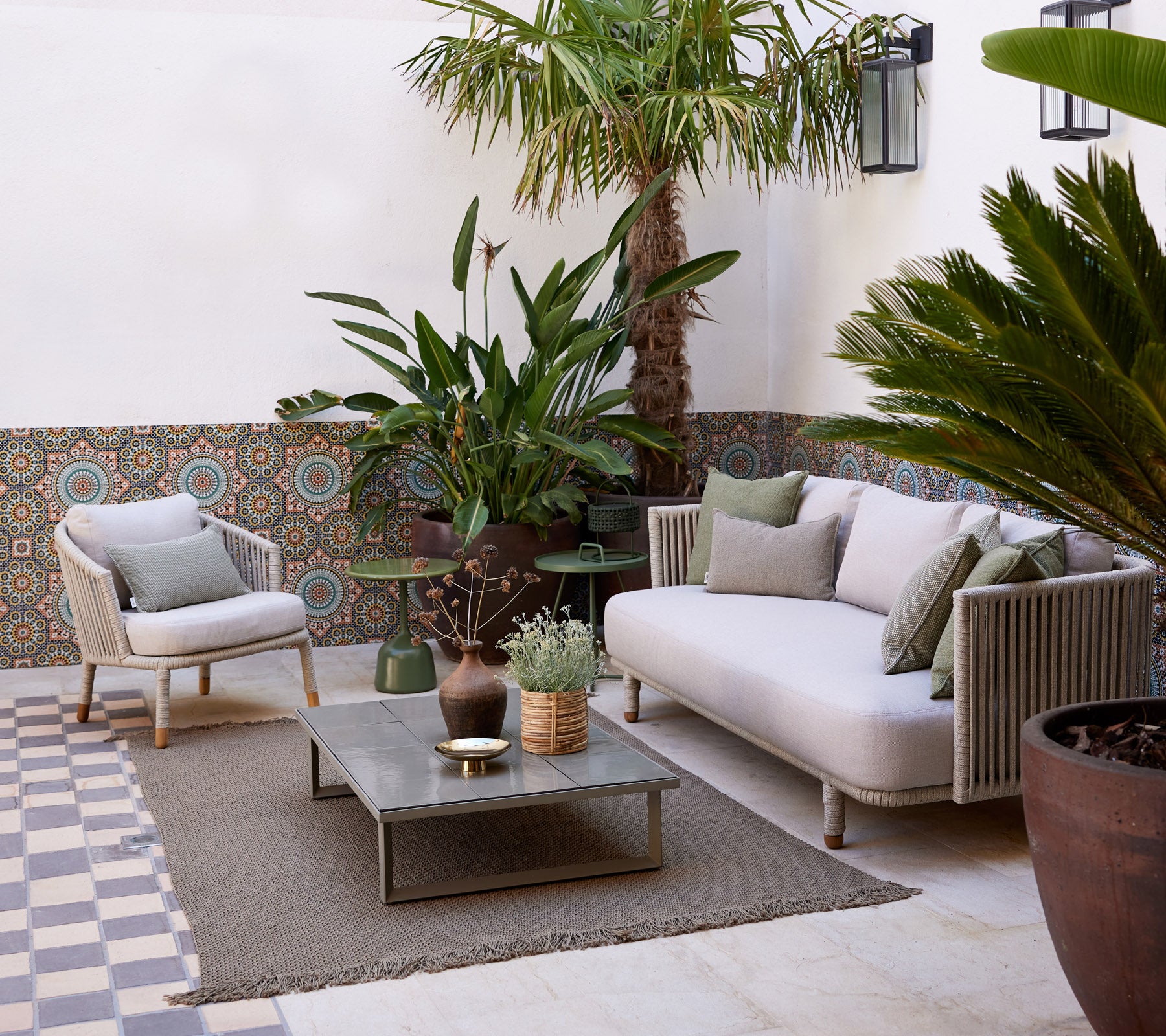 Zona de salón acogedora con un sofá claro, plantas en macetas, mesa decorativa y suelo texturizado, creando una atmósfera serena.