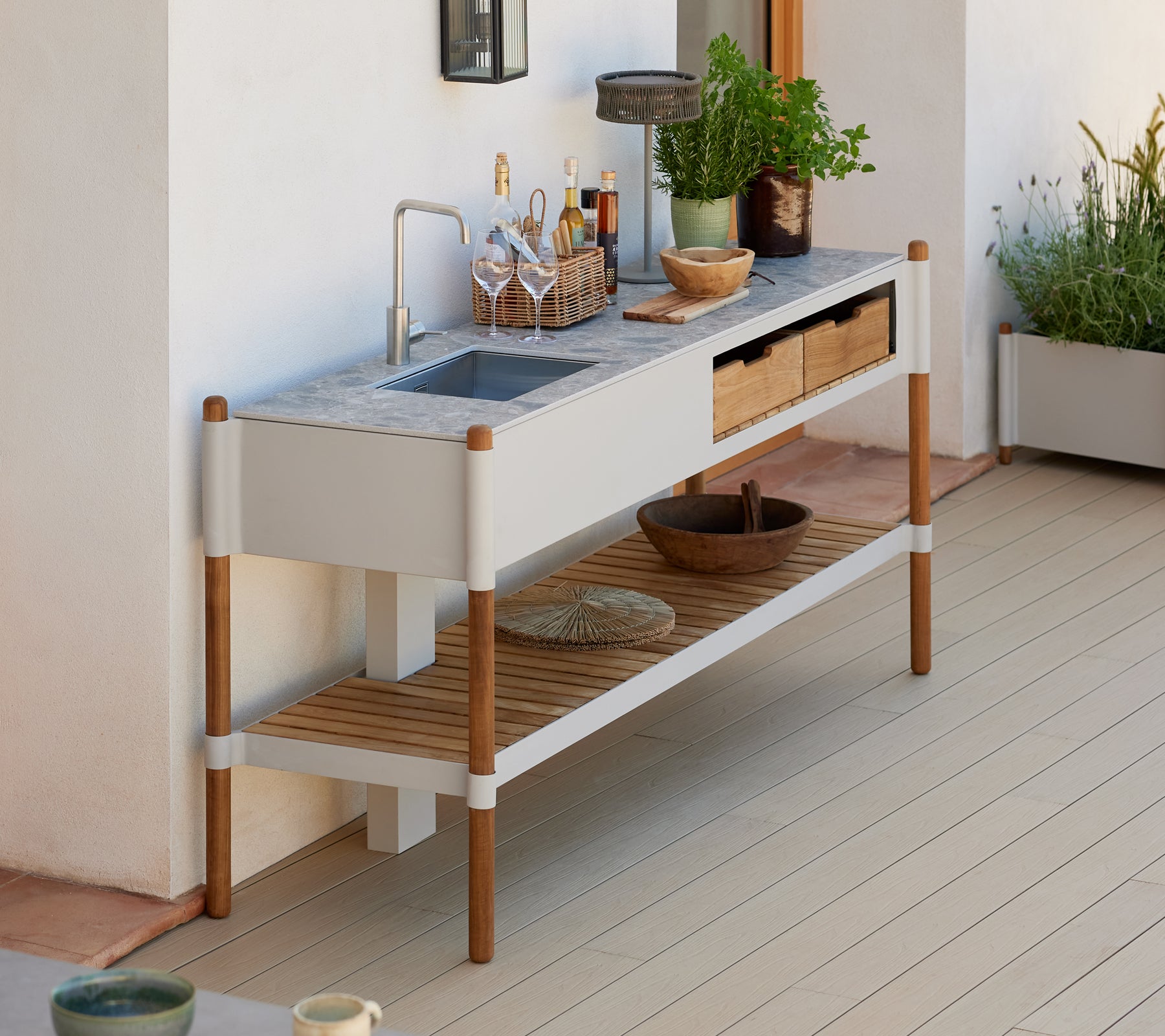 Una estación de fregadero al aire libre moderna y minimalista con una encimera de granito, cajones de almacenamiento de madera y arreglos de plantas decorativas.