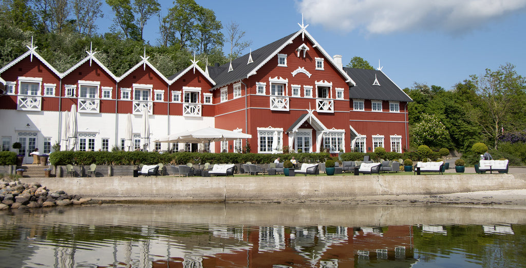 Dyvig Badehotel hotelbuilding in red and white exterior, outdoor lounge area in the foreground, sea view