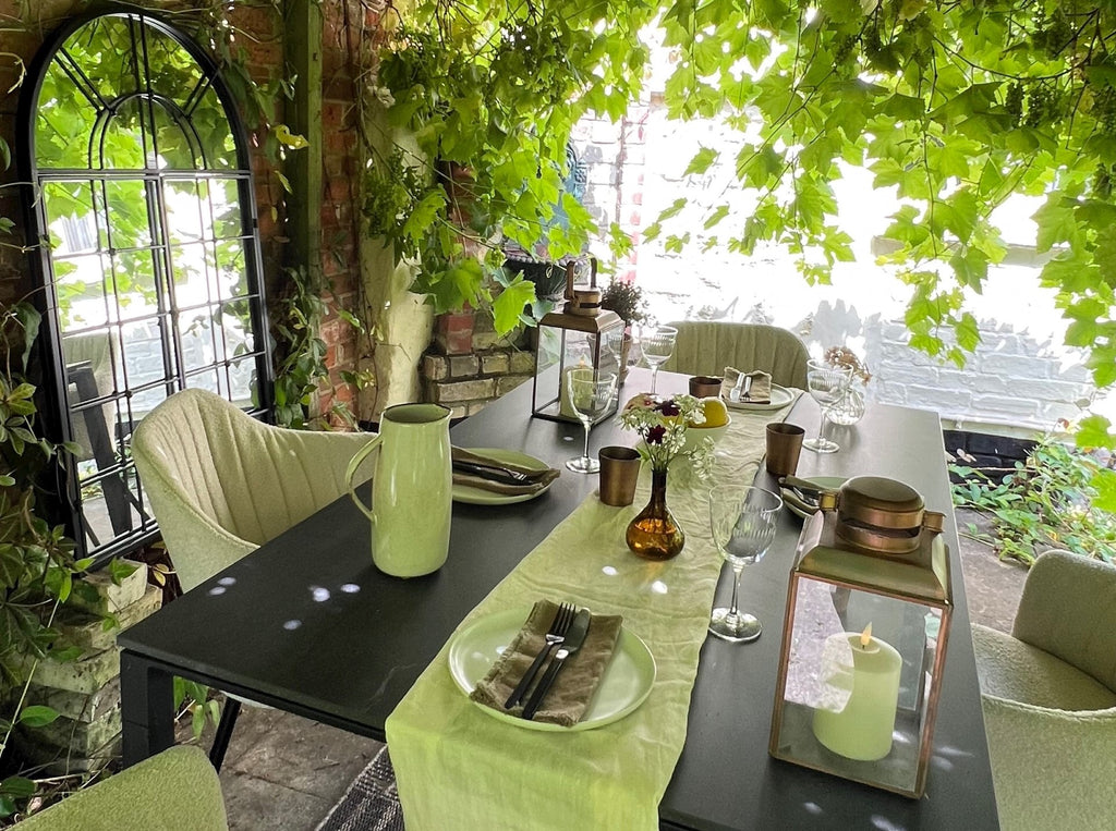 Pergola with green grapevines, dining setting with sand bouclé outdoor chairs, black ceramic outdoor dining table 150x90 cm