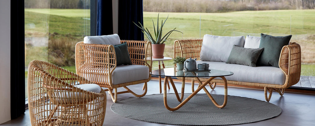 A cozy seating arrangement featuring woven lounge chairs and a stylish glass table, with decorative cushions and a potted plant.