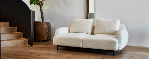 Sofá moderno y acogedor de dos plazas con cojines suaves sobre un elegante marco de metal, acompañado de una maceta estilosa y decoración minimalista.