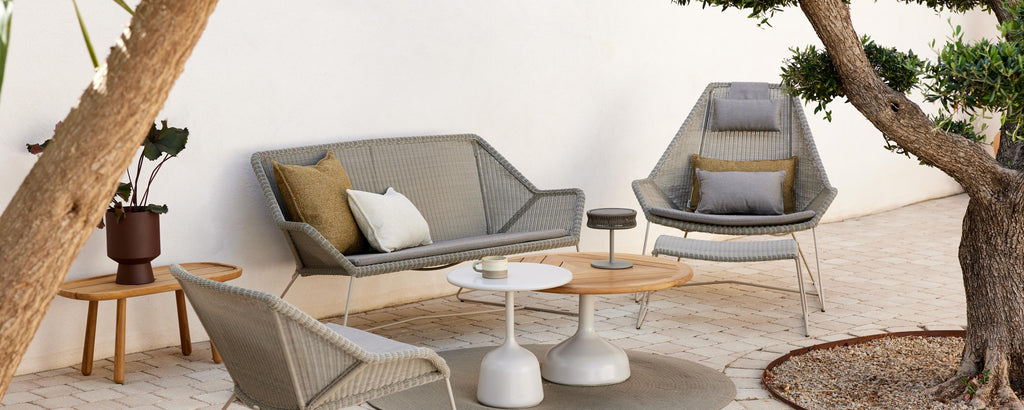 Modern seating arrangement featuring a gray sofa, accent chair, and a wooden table, surrounded by natural elements and soft cushions.