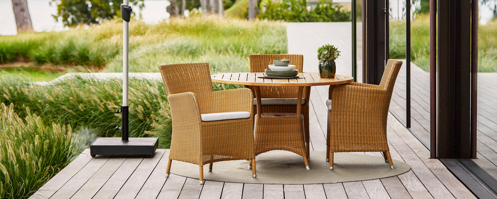 Stylish wicker dining set with four chairs and a round table, complemented by a decorative plant and a sleek outdoor heater.