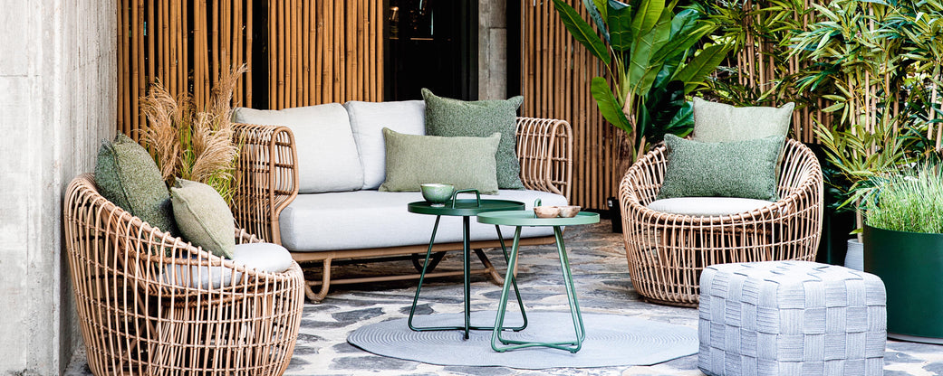 Stylish seating arrangement featuring woven furniture, cushions, a coffee table, and greenery for a cozy atmosphere.