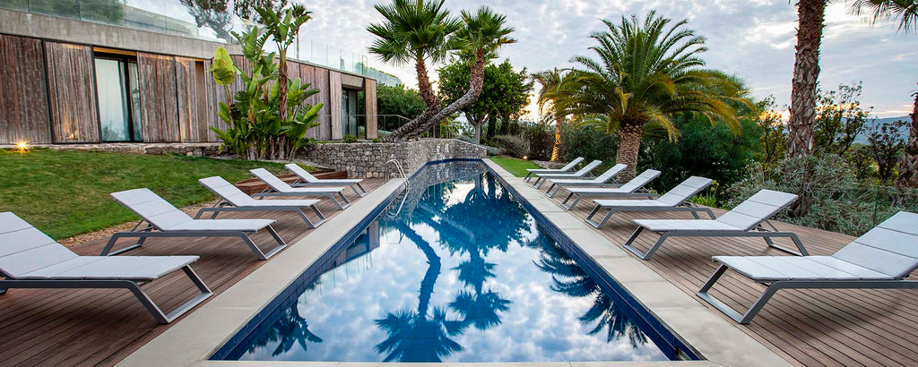 Serene scene featuring a swimming pool surrounded by lounge chairs and tropical greenery, reflecting palm trees in the water. Perfect for relaxation.