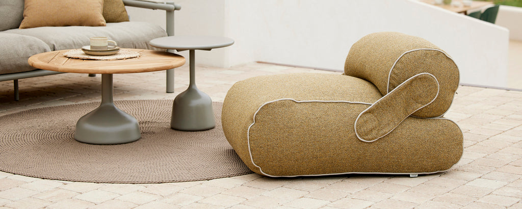 A modern, curved lounge chair in a warm tone, paired with a minimalist wooden table on a round rug, creating a cozy and stylish seating arrangement.