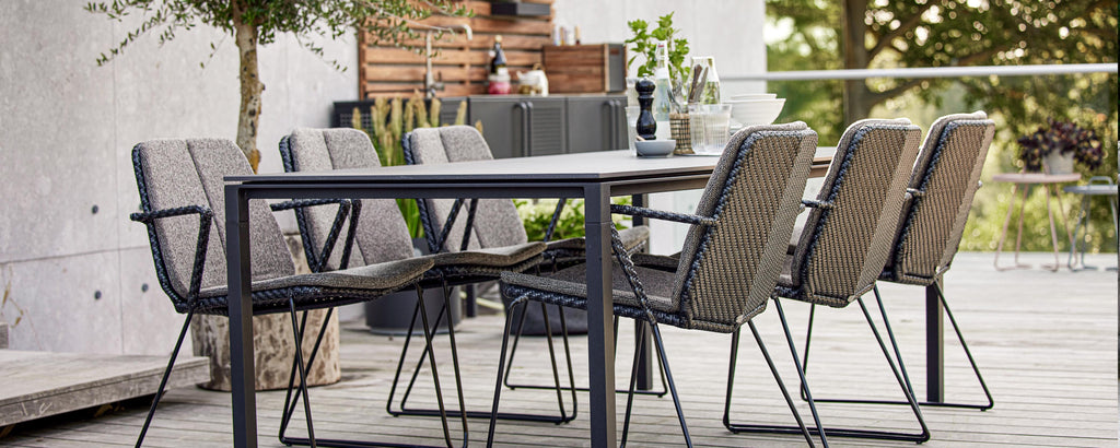 A modern dining table set featuring a sleek table and multiple stylish chairs, surrounded by greenery. Perfect for gatherings.