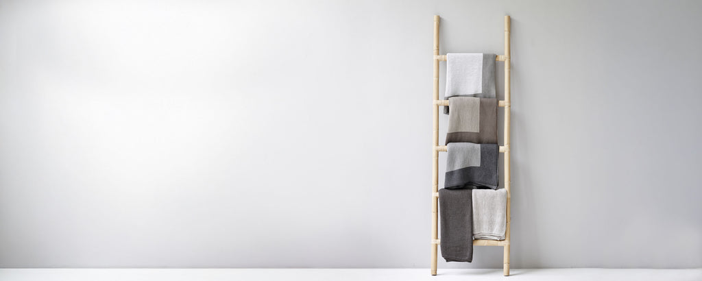 A wooden ladder displaying various folded cloths in neutral tones against a simple background.