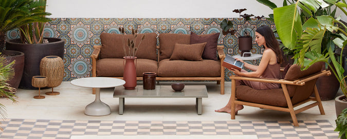 Una zona de estar acogedora con sillones marrones, una mesa de café, plantas y azulejos decorativos en la pared, creando un ambiente relajado.