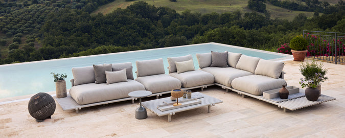 Una disposición elegante de sofás modulares con cojines, acompañada de una mesa de café y plantas, frente a un hermoso fondo natural.