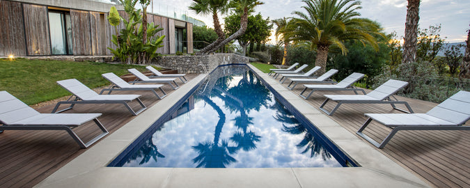 Una escena serena junto a la piscina con una fila de tumbonas blancas junto a un agua tranquila, rodeada de exuberante vegetación y palmeras.