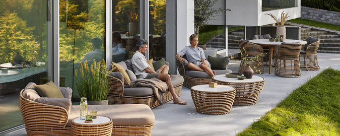 Sillas de ratán modernas con cojines grises y una mesa de café en un entorno de salón exterior contemporáneo.