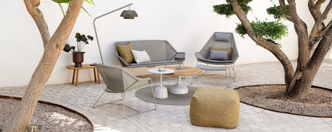 Configuración moderna de sala de estar con un sofá gris, una silla gris, una mesa de café de madera y un puff amarillo.