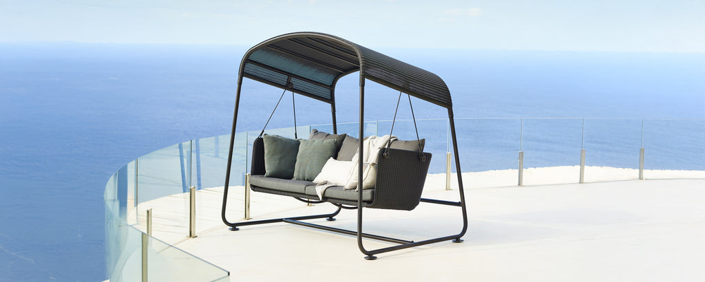 Silla de columpio moderna con cojines grises y marco negro con vistas a un paisaje escénico.