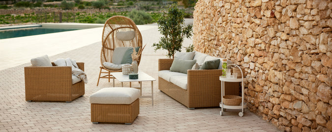 Configuración moderna de salón exterior con sofá de ratán marrón y sillas con cojines beige.