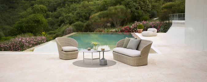 Sofá gris moderno con cojines y mesa redonda junto a la piscina.