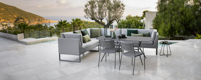 Moderno área de salón al aire libre con sofá gris, cojines verdes, mesa negra y sillas grises.