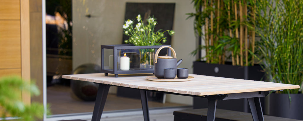 Mesa moderna con linterna negra, tetera y taza rodeadas de verdor.