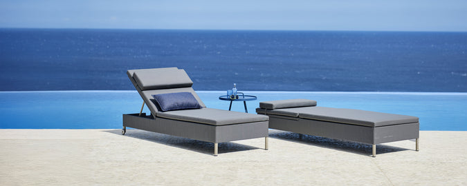 Sillón lounge gris y chaise longue junto a una piscina con vista al océano.