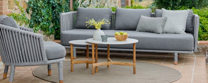 Moderno área de salón al aire libre con un sofá gris, una silla gris y una mesa de café de madera.