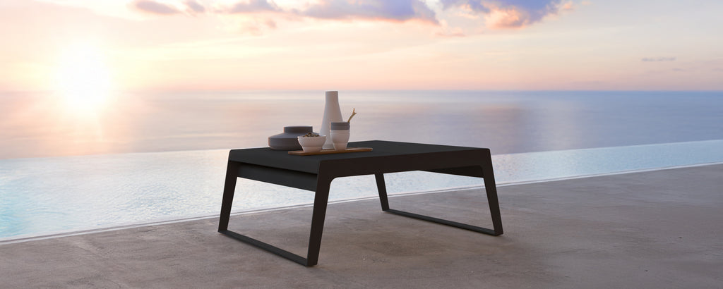 Mesa negra moderna en una terraza con vista al atardecer sobre el agua.