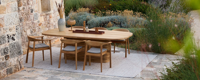 Mesa de comedor de madera con sillas de madera y cojines grises en un entorno al aire libre.