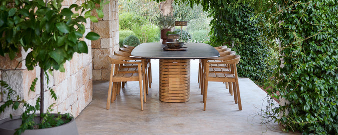 Sillas de comedor de madera al aire libre alrededor de una mesa negra en un jardín verde.