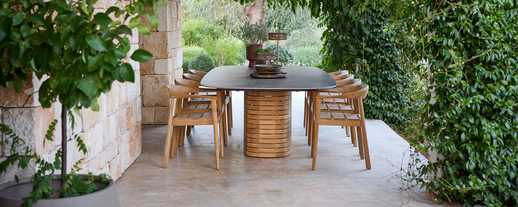 Sillas de comedor de madera al aire libre alrededor de una mesa negra en un jardín verde.