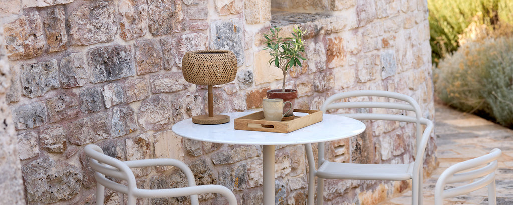 Configuración moderna al aire libre con mesa blanca, sillas blancas y elementos decorativos marrones.