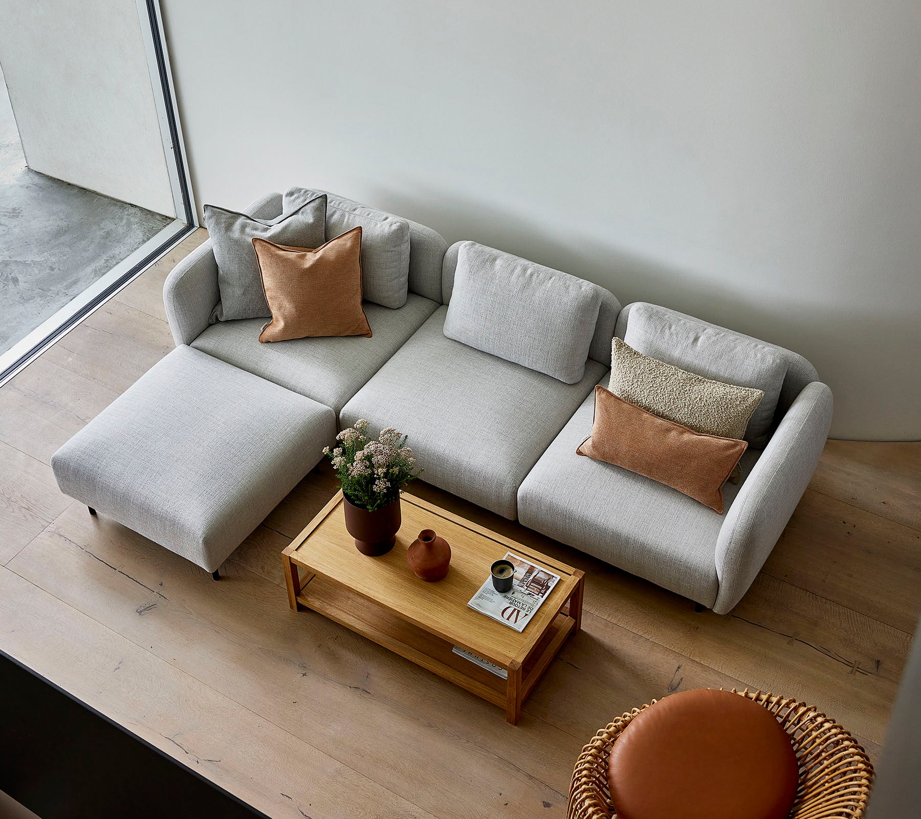 Un sofá seccional gris claro y elegante con cojines, acompañado de una mesa de centro de madera y una opción de asiento redonda, creando una atmósfera acogedora.