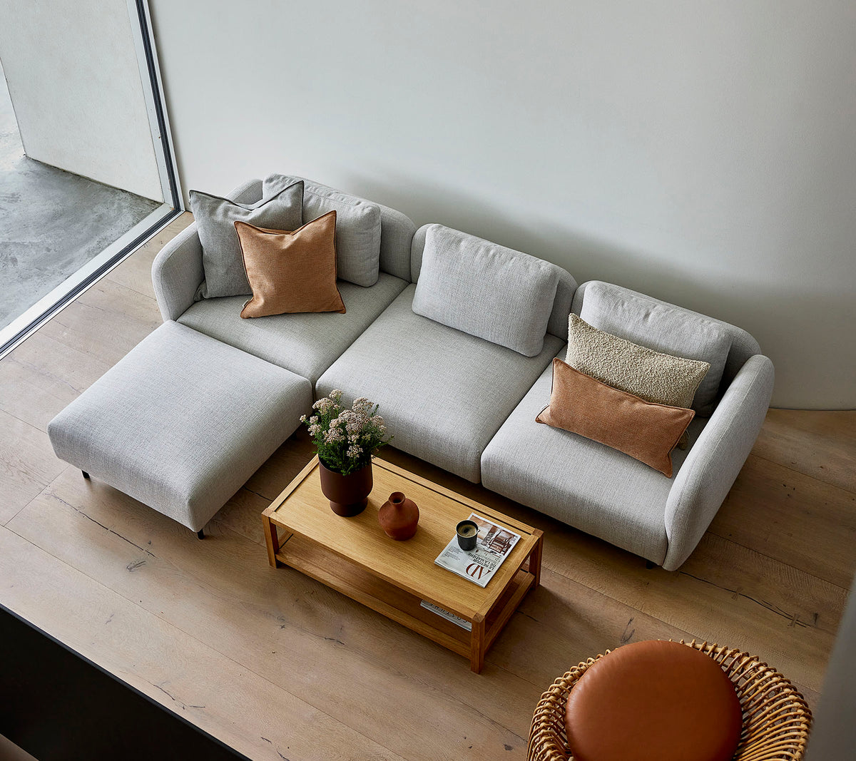 Un sofá seccional gris claro y elegante con cojines, acompañado de una mesa de centro de madera y una opción de asiento redonda, creando una atmósfera acogedora.