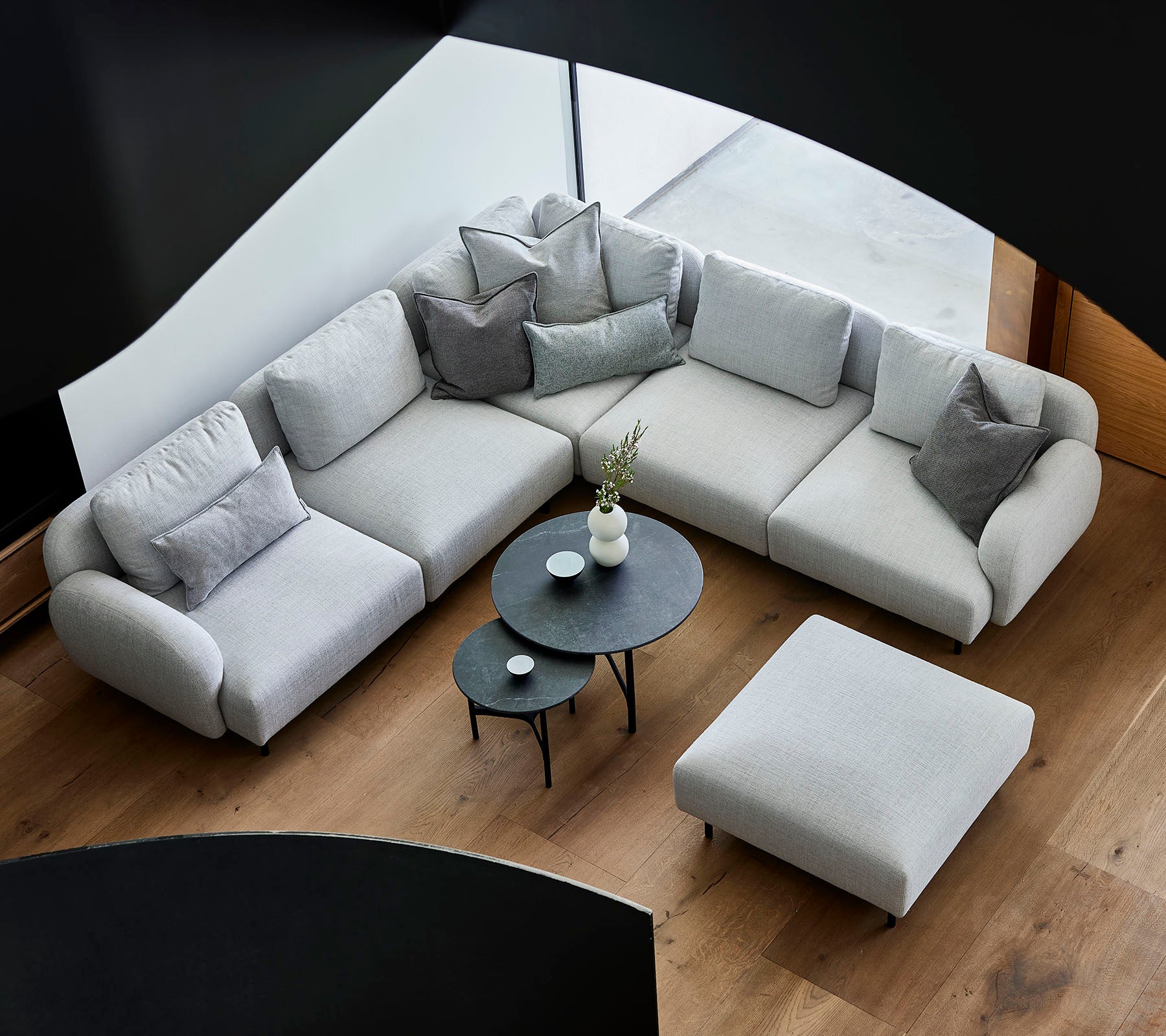 Sofá seccional gris elegante con cojines decorativos, acompañado de una mesa de café redonda elegante y un ottoman en un suelo de madera.