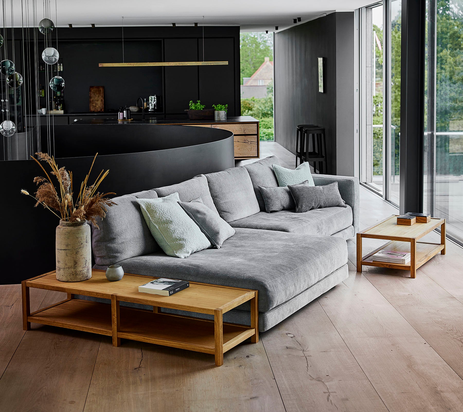 Espacio de vida moderno con un sofá seccional gris adornado con cojines, complementado con mesas auxiliares de madera y arreglos de plantas decorativas.