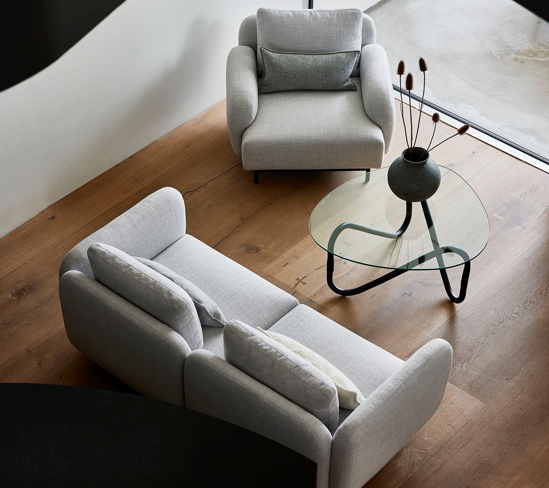 Sofás grises elegantes y una mesa de café de vidrio elegante, con elementos decorativos en la parte superior, contra un cálido suelo de madera.