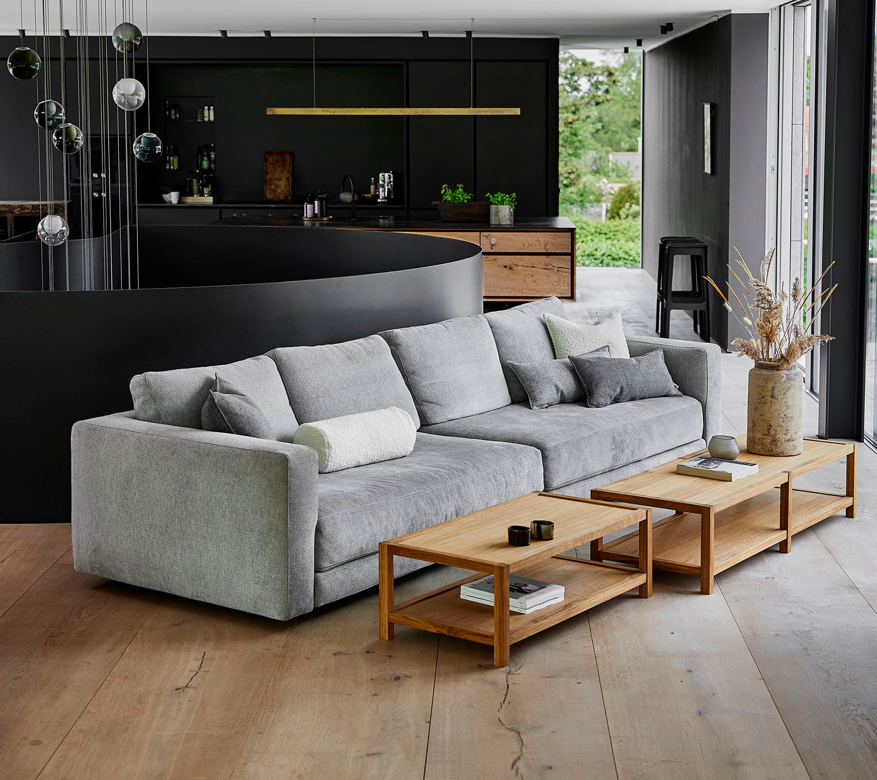 Un sofá moderno, gris, con cojines mullidos al lado de mesas de café de madera en un entorno contemporáneo con una decoración elegante.