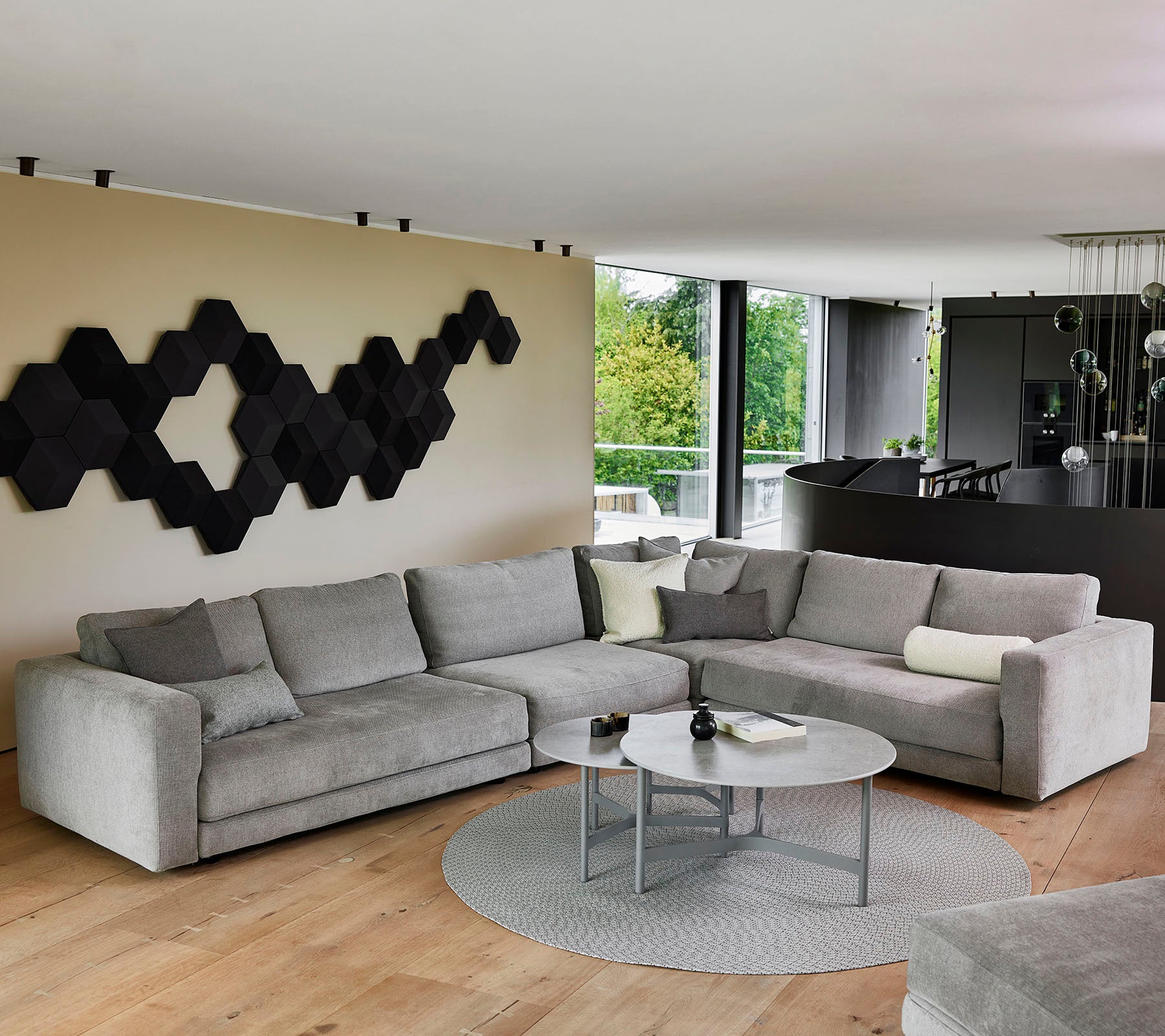 Un sofá seccional gris moderno con cojines decorativos, una mesa de café redonda y una pieza de arte mural texturizada en negro.