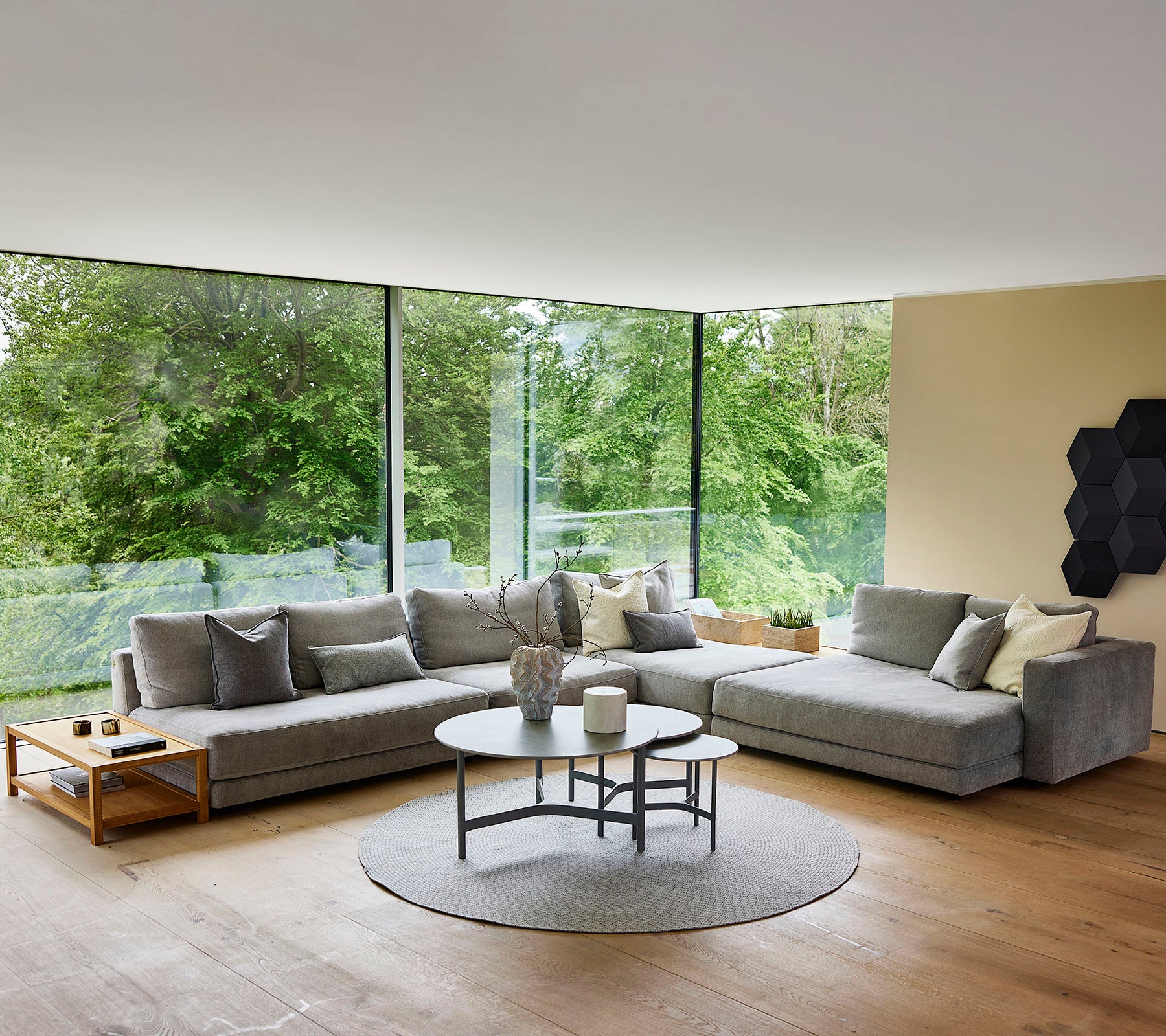 Un espacio de vida moderno que cuenta con un sofá seccional gris, una mesa de café redonda y grandes ventanas que realzan la luz natural.