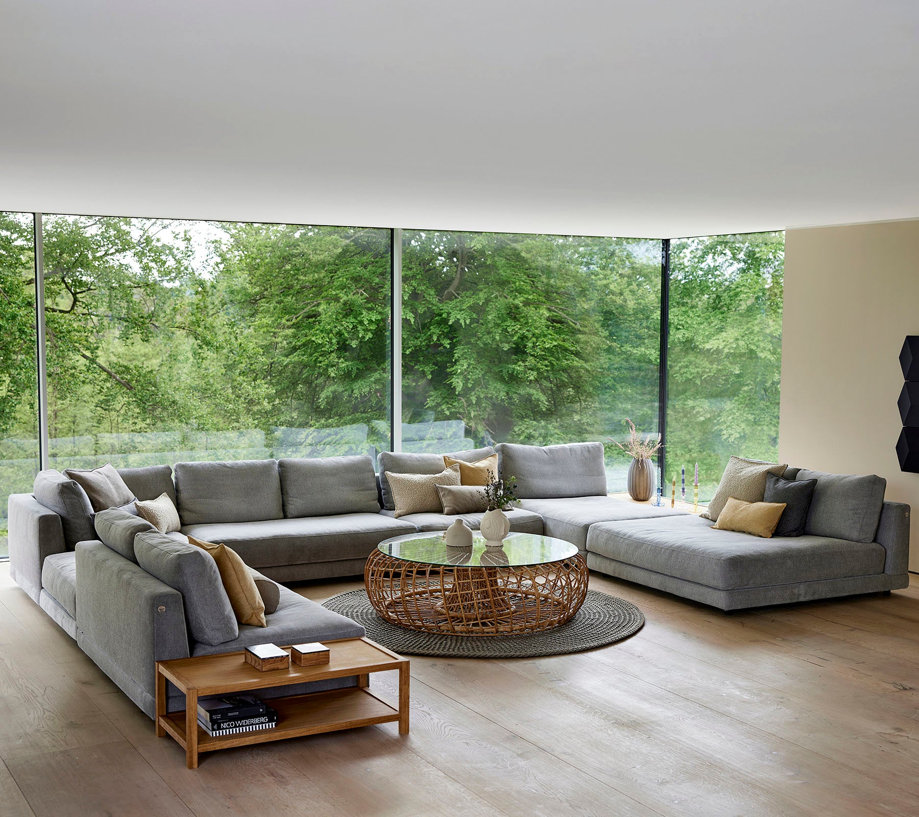 Amplia sala de estar con un gran sofá en forma de L, mesa de café y acentos decorativos, rodeada de luz natural y vegetación.