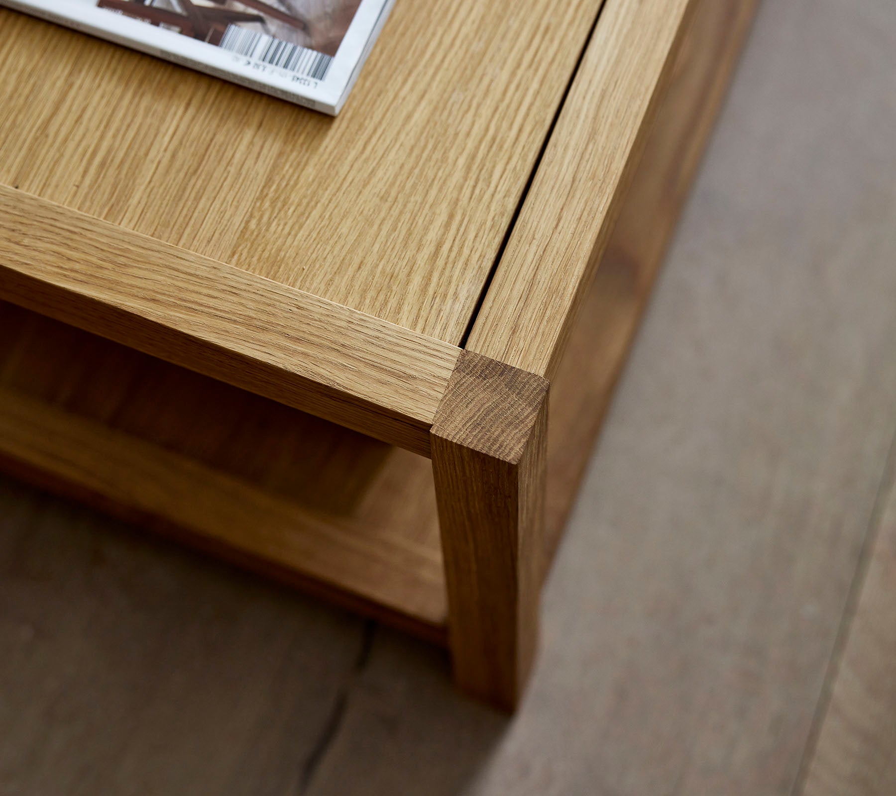 Mesa de café de madera con un diseño limpio, que cuenta con una revista colocada encima y una estantería inferior minimalista para almacenamiento adicional.
