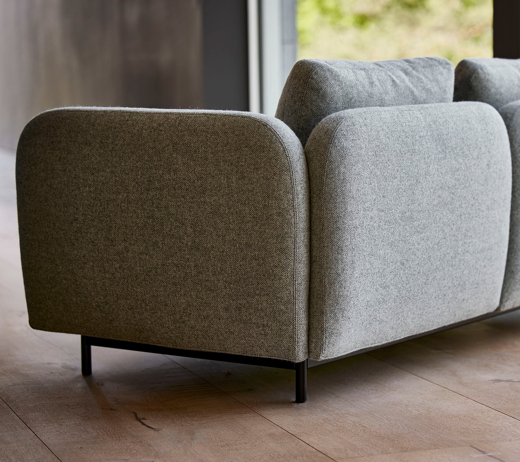Un sofá moderno tapizado en gris con bordes redondeados y patas negras elegantes, que muestra un diseño minimalista.