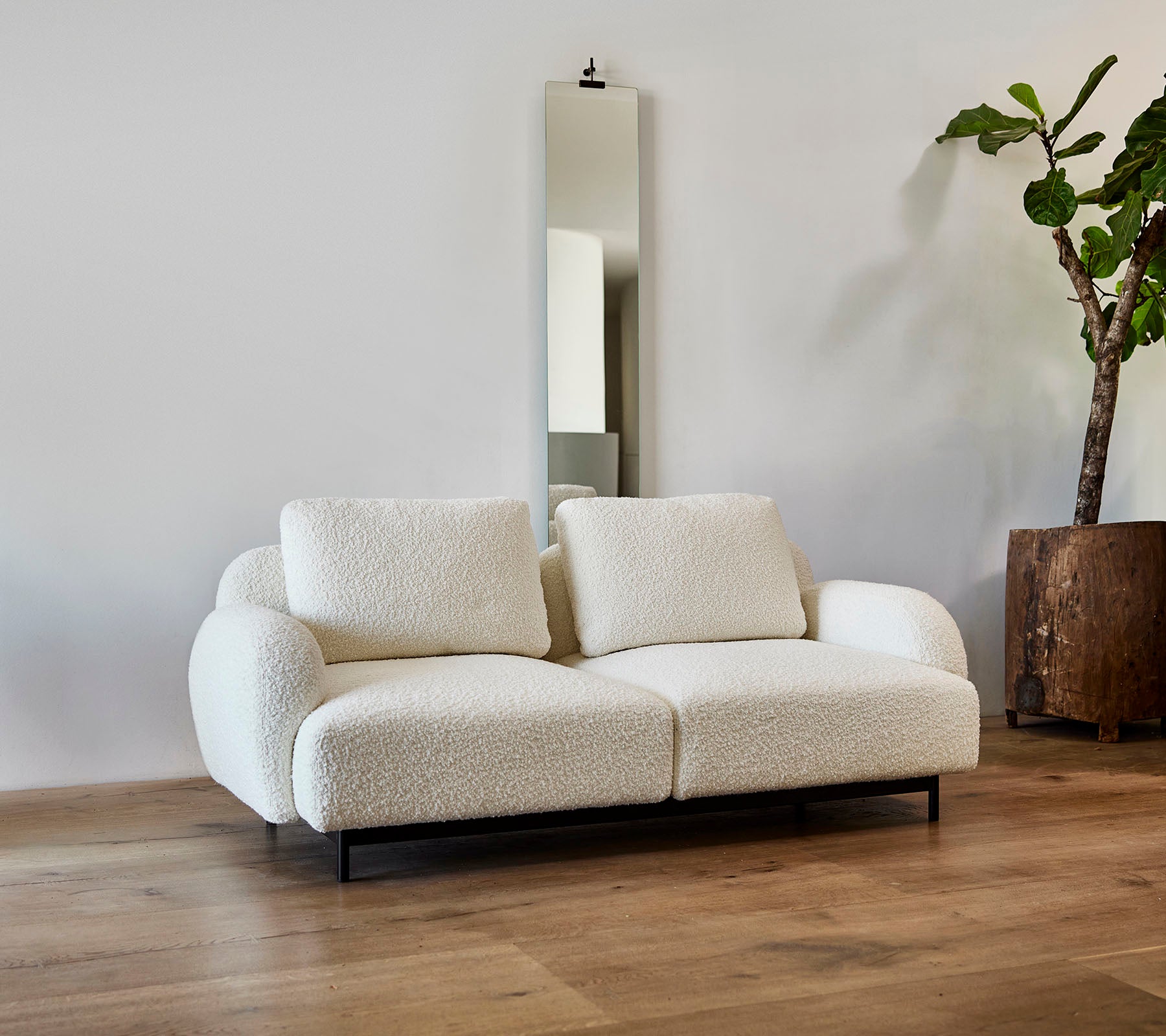 Un sofá blanco elegante con cojines mullidos, acompañado de un gran espejo y una planta en maceta en un entorno moderno.