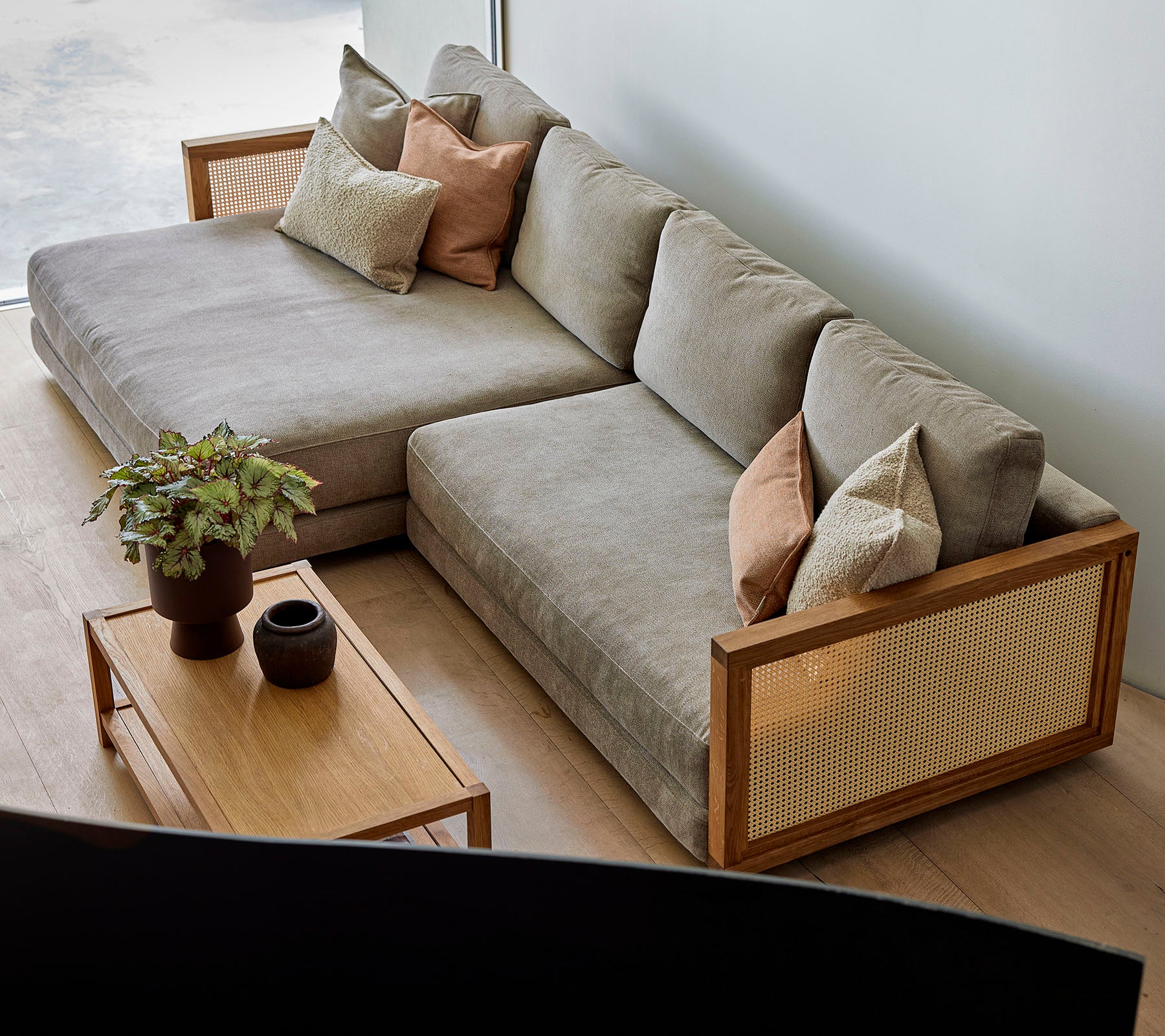 Un sofá seccional elegante con cojines suaves y almohadas decorativas, combinado con una mesa de café de madera con plantas y decoración elegante.