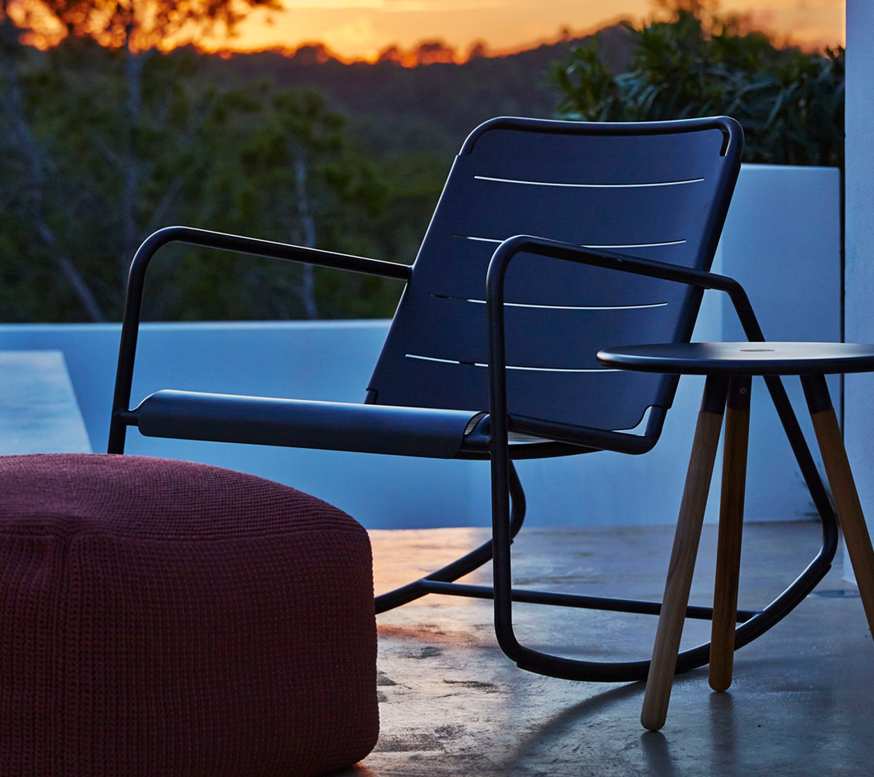 Sillón mecedora elegante con un marco negro elegante y un cojín de asiento gris, acompañado de una pequeña mesa de madera y un pouf redondo.