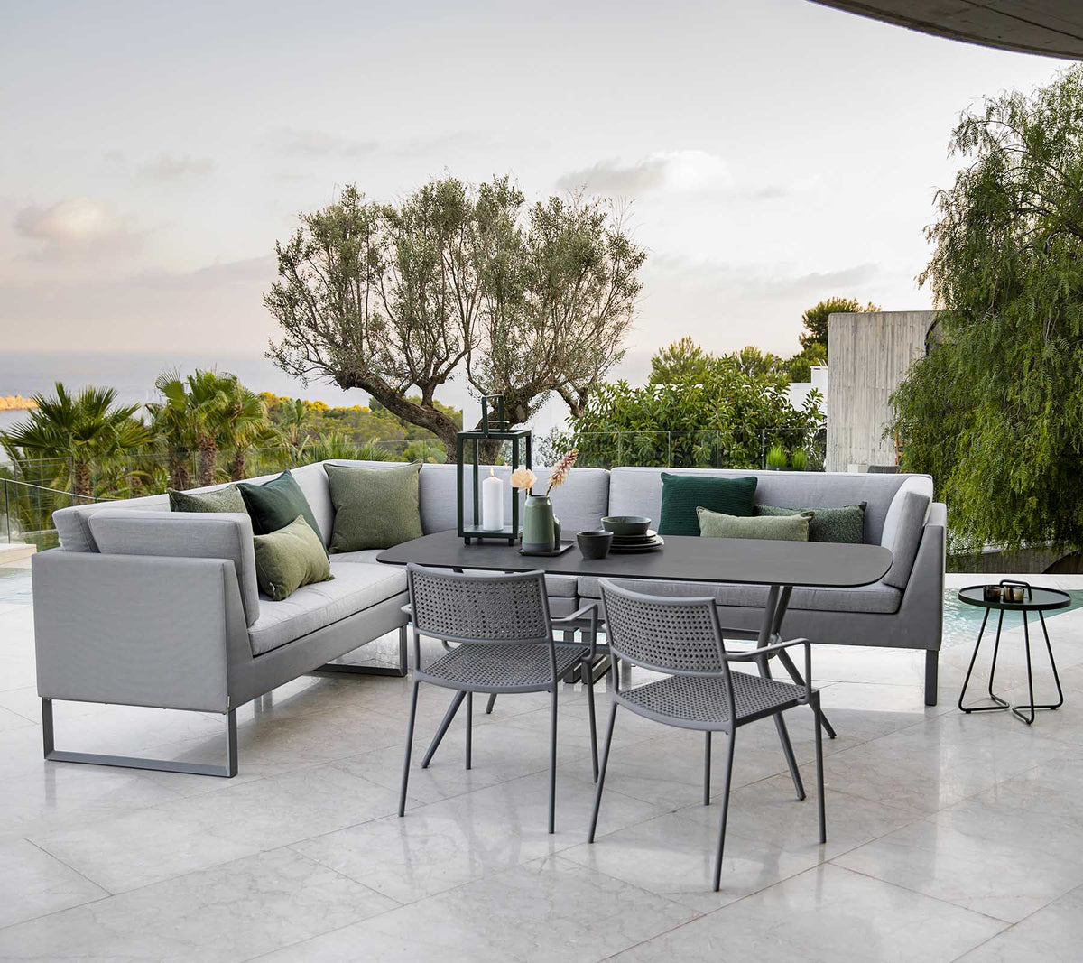 Moderna zona de estar al aire libre con un sofá seccional elegante, una mesa de comedor y sillas de metal rodeadas de vegetación.