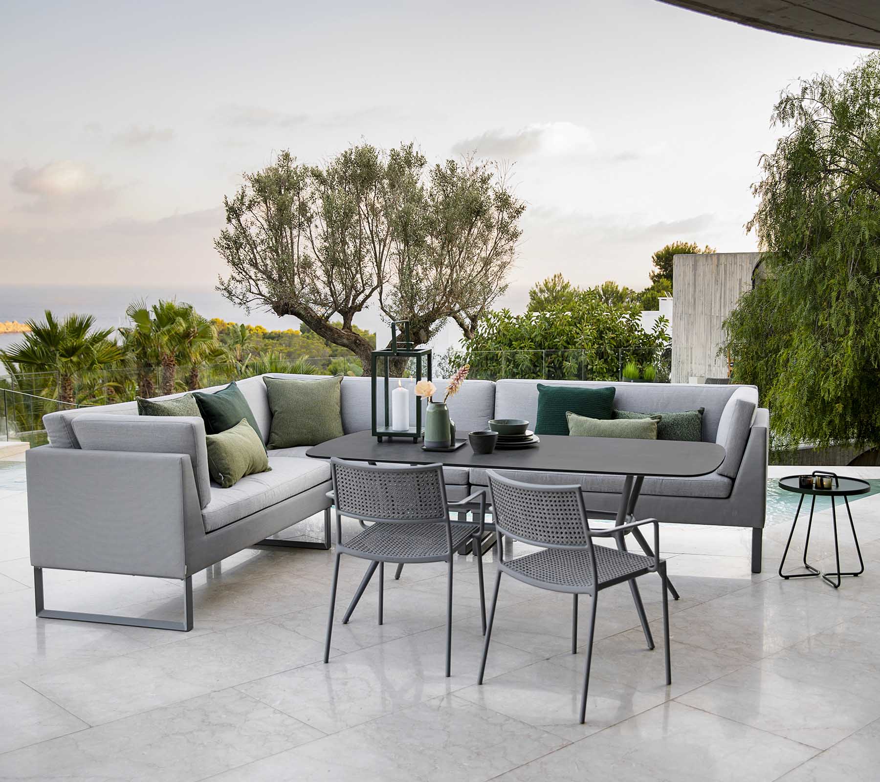 Moderna zona de estar al aire libre con un sofá seccional elegante, una mesa de comedor y sillas de metal rodeadas de vegetación.