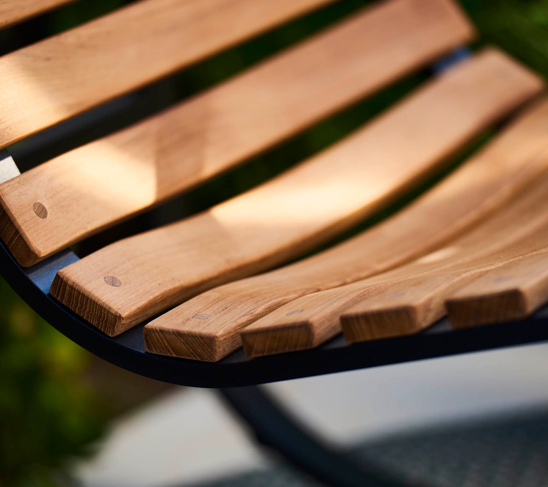 Primer plano de una tabla de banco de madera curvada con vetas de madera naturales y suaves, que muestra la artesanía y un diseño cálido y acogedor.