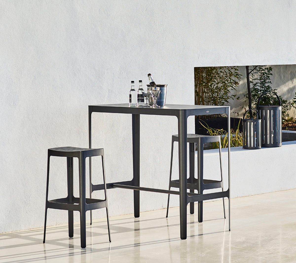 Una mesa elegante con dos taburetes a juego, con un diseño minimalista y botellas colocadas encima, contra un fondo neutro.